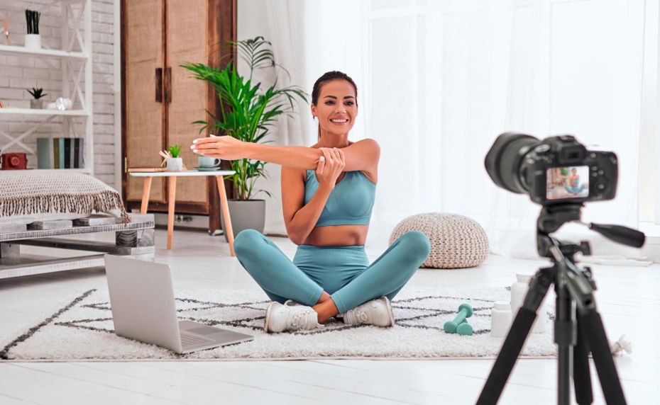 Female trainer sitting on carpet stretching in front of camera live streaming