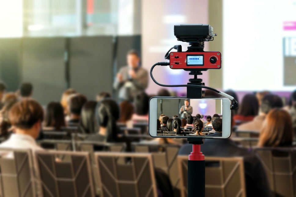 Man Live Streaming a Lecture from mobile device in front of seated audience